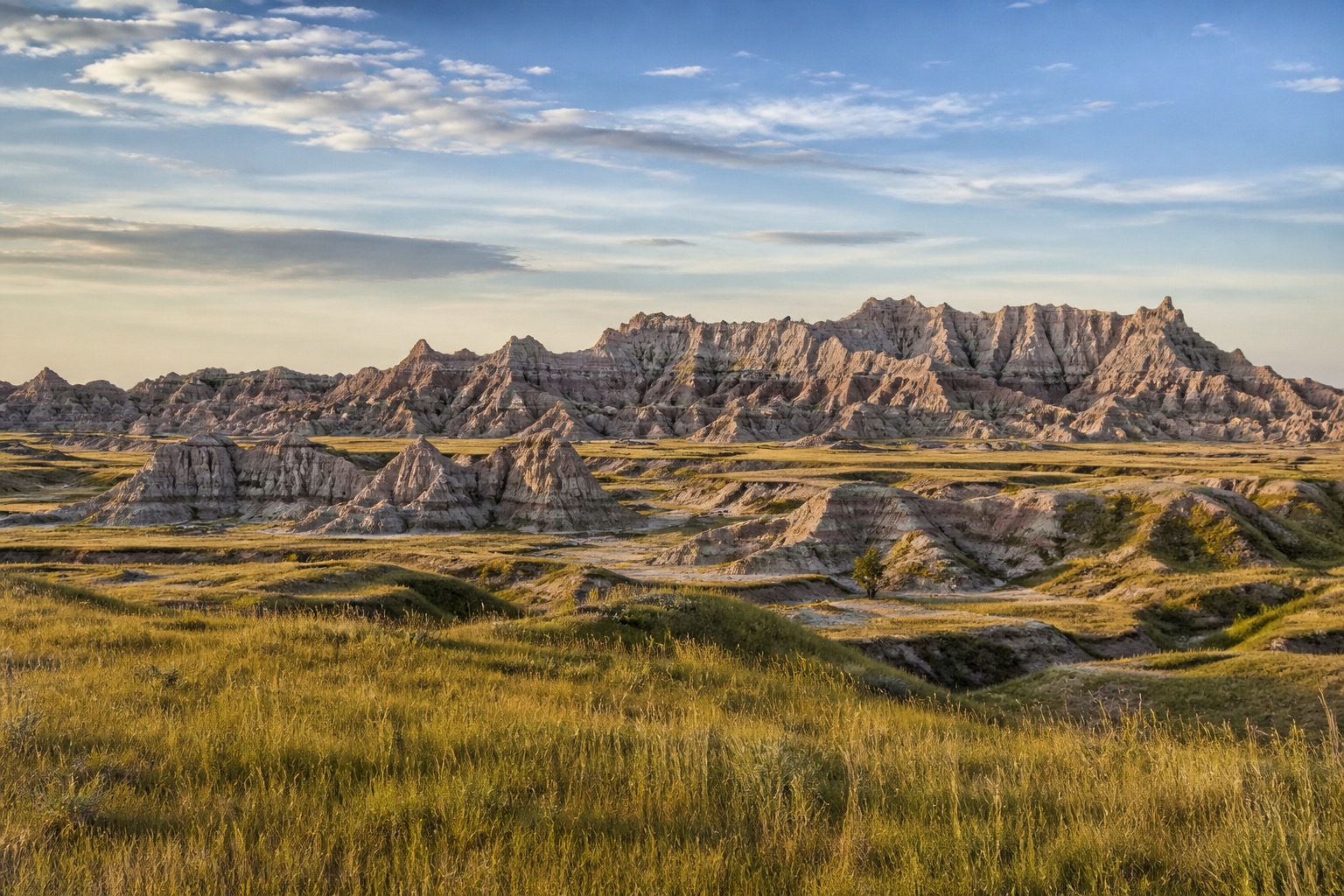Badlands layered formations and mixed-grass prairie beneath a broad natural morning sky
