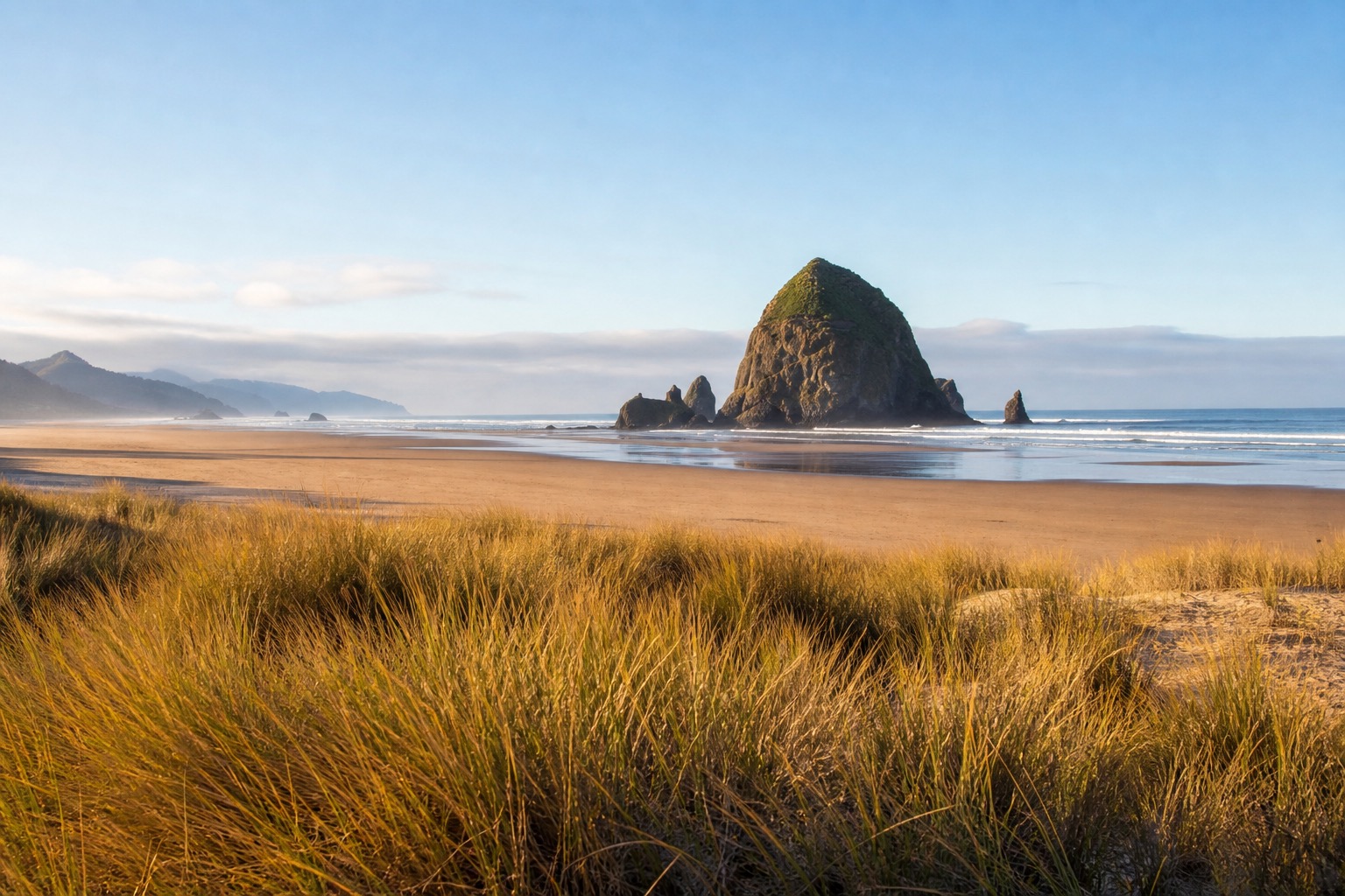 Haystack Rock at Cannon Beach with broad wet sand and a clear Oregon coast morning