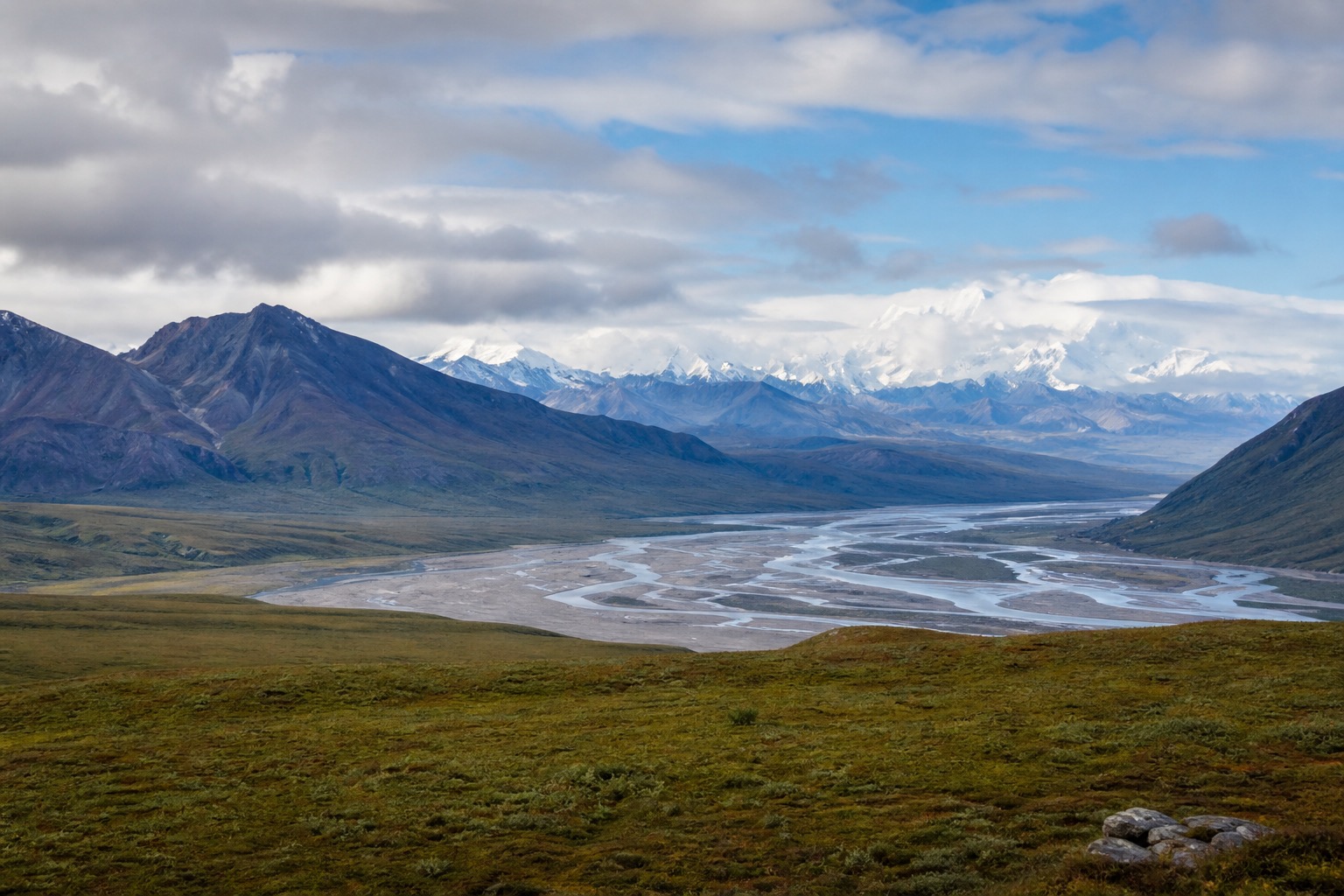 Denali tundra and braided river valley beneath a vast Alaska Range in natural light