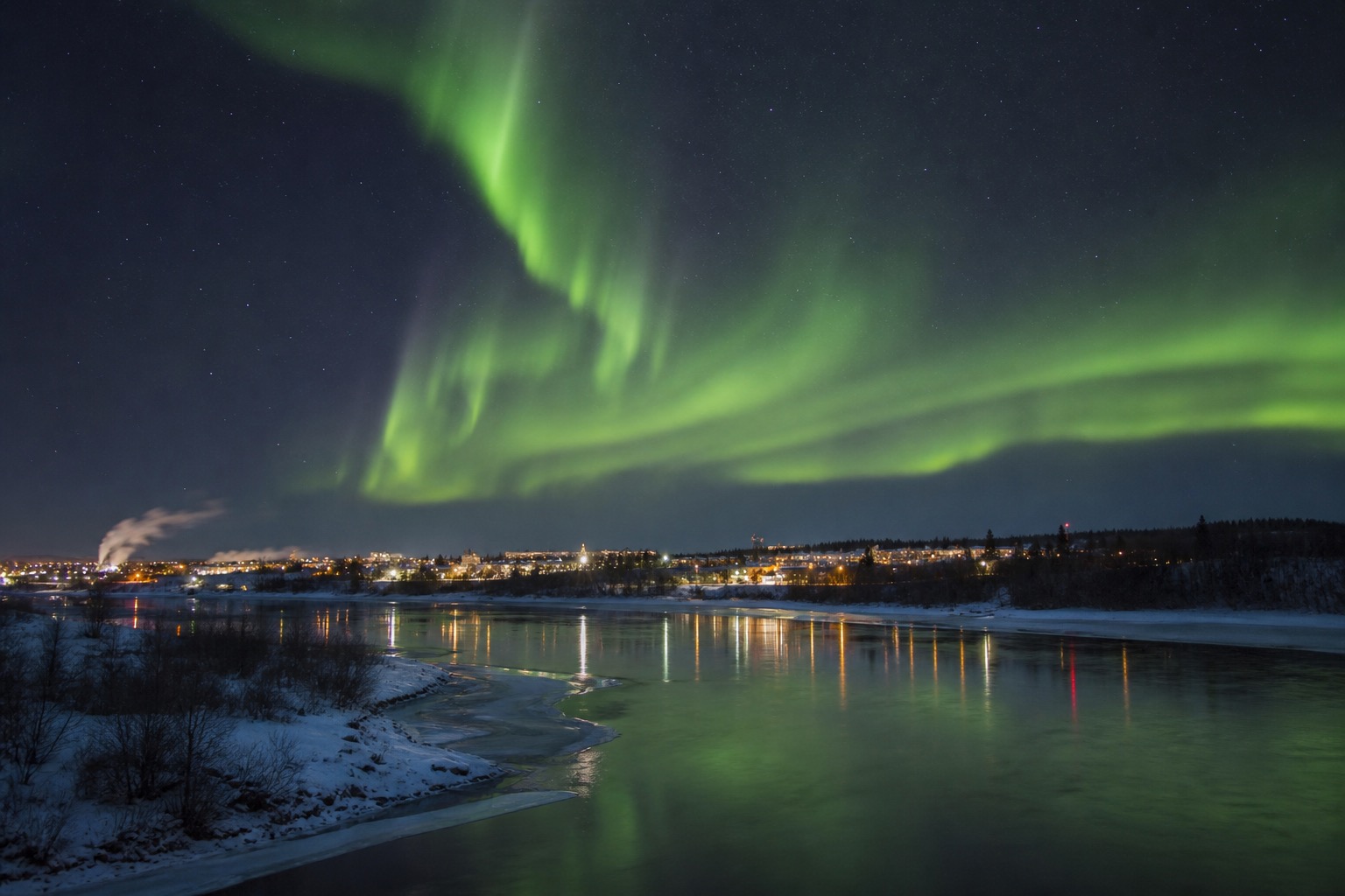 Fairbanks beneath a clear aurora sky with the Chena River and winter lights