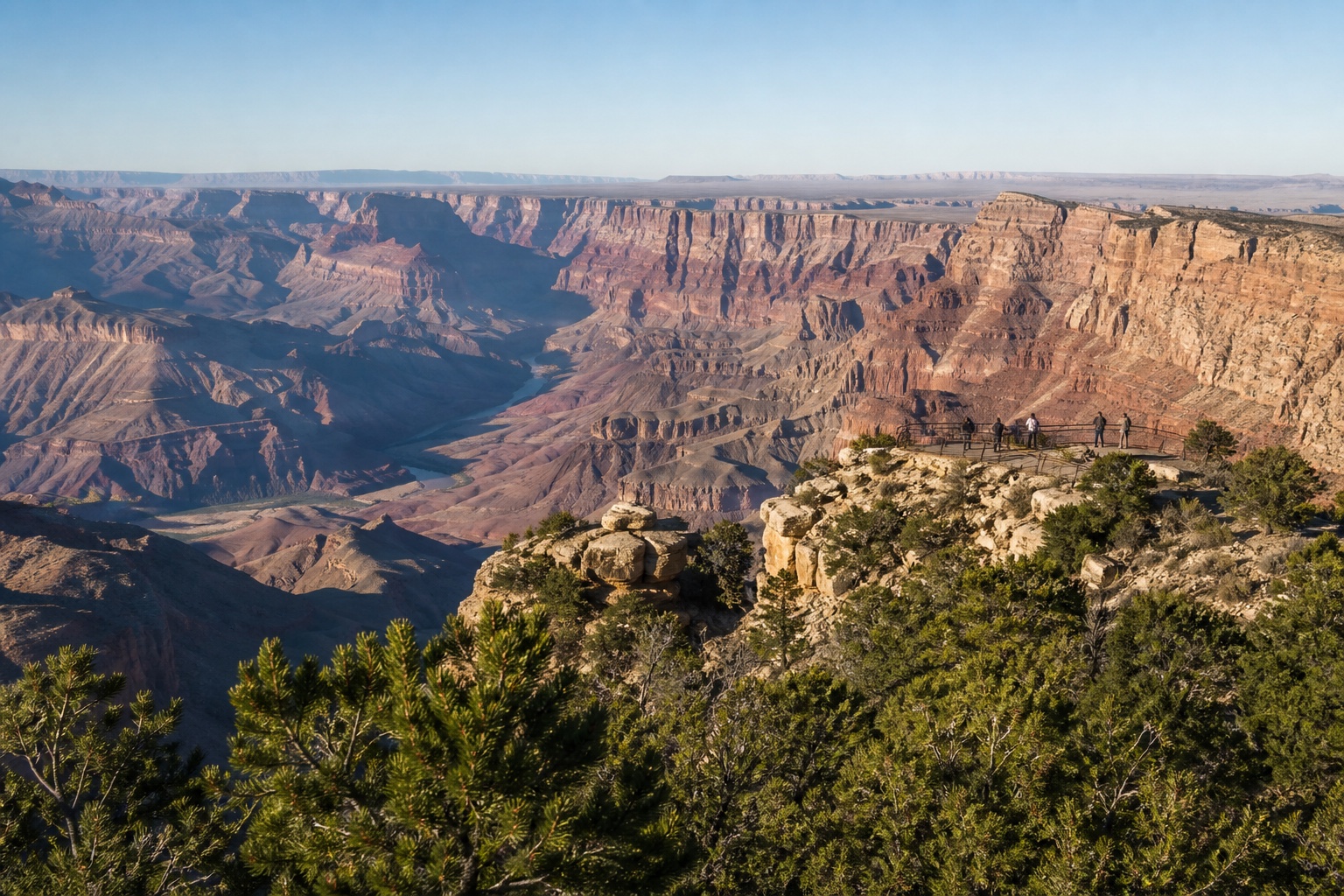 The layered Grand Canyon and Colorado River from a protected South Rim overlook in morning light