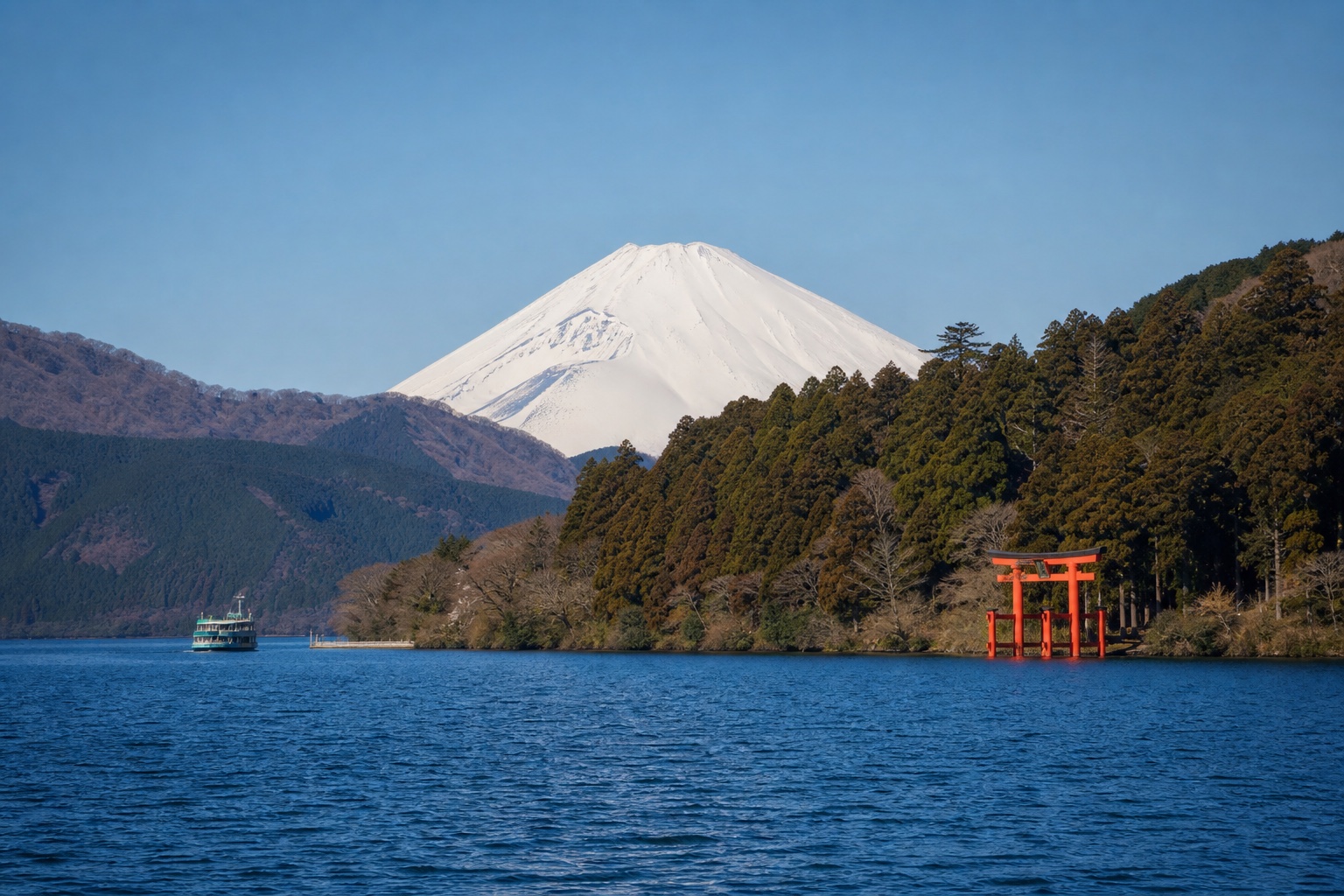 Lake Ashi, wooded Hakone hills, lakeside torii, a small boat, and Mount Fuji under clear conditions