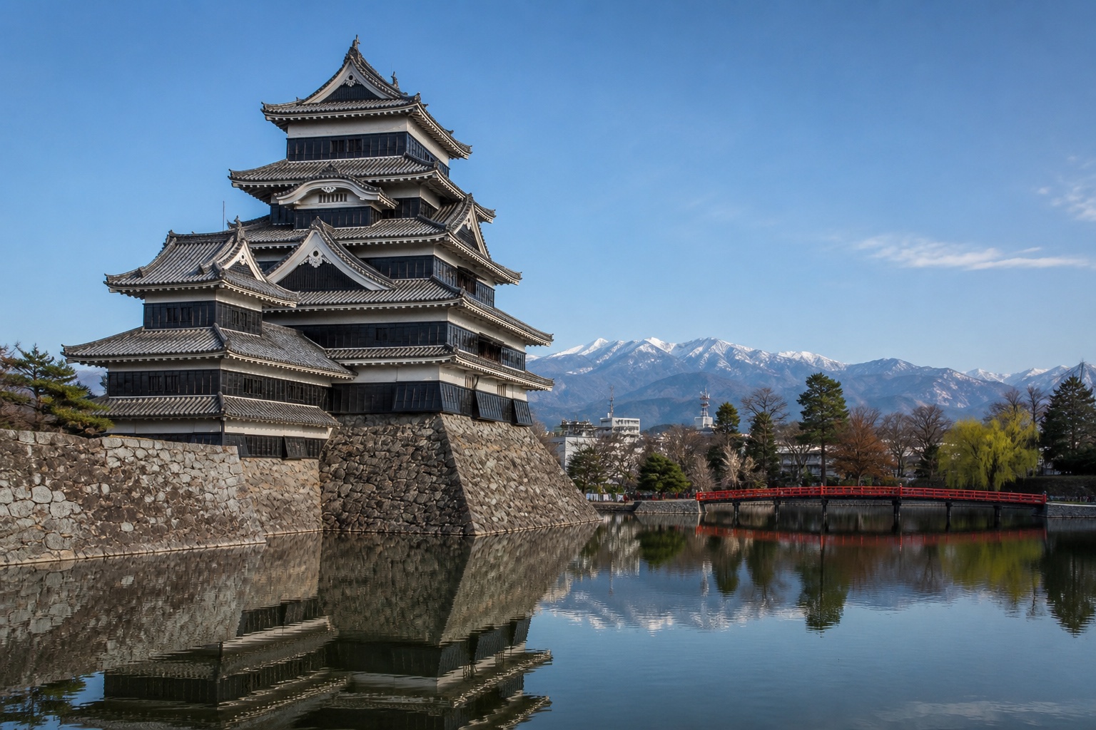 Matsumoto Castle's black-and-white keep reflected in its moat with the Japanese Alps beyond