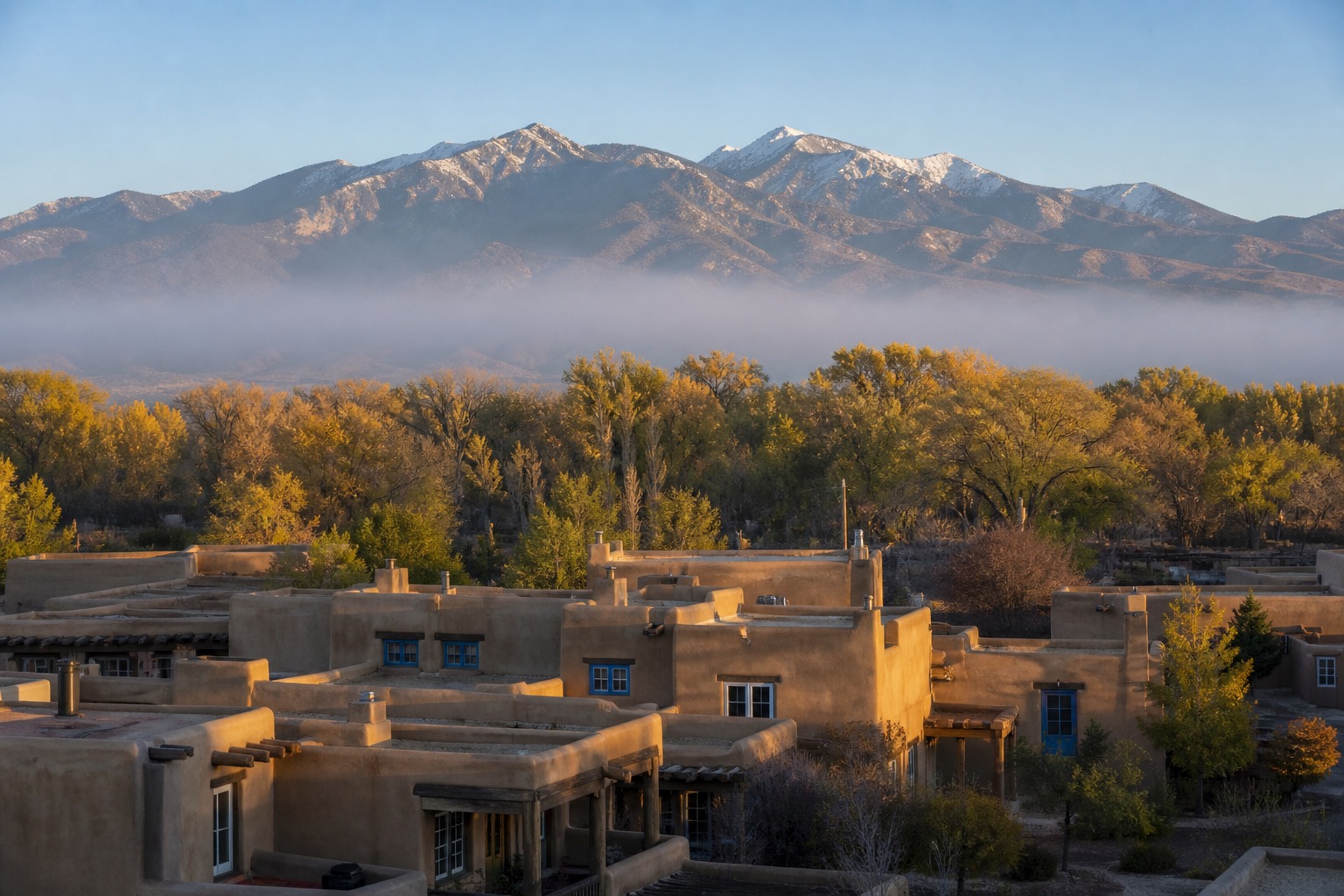Taos adobe buildings with cottonwoods and Sangre de Cristo peaks in clear high-desert light